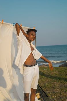 Stylish young man posing with white fabric backdrop at the beach in Accra.