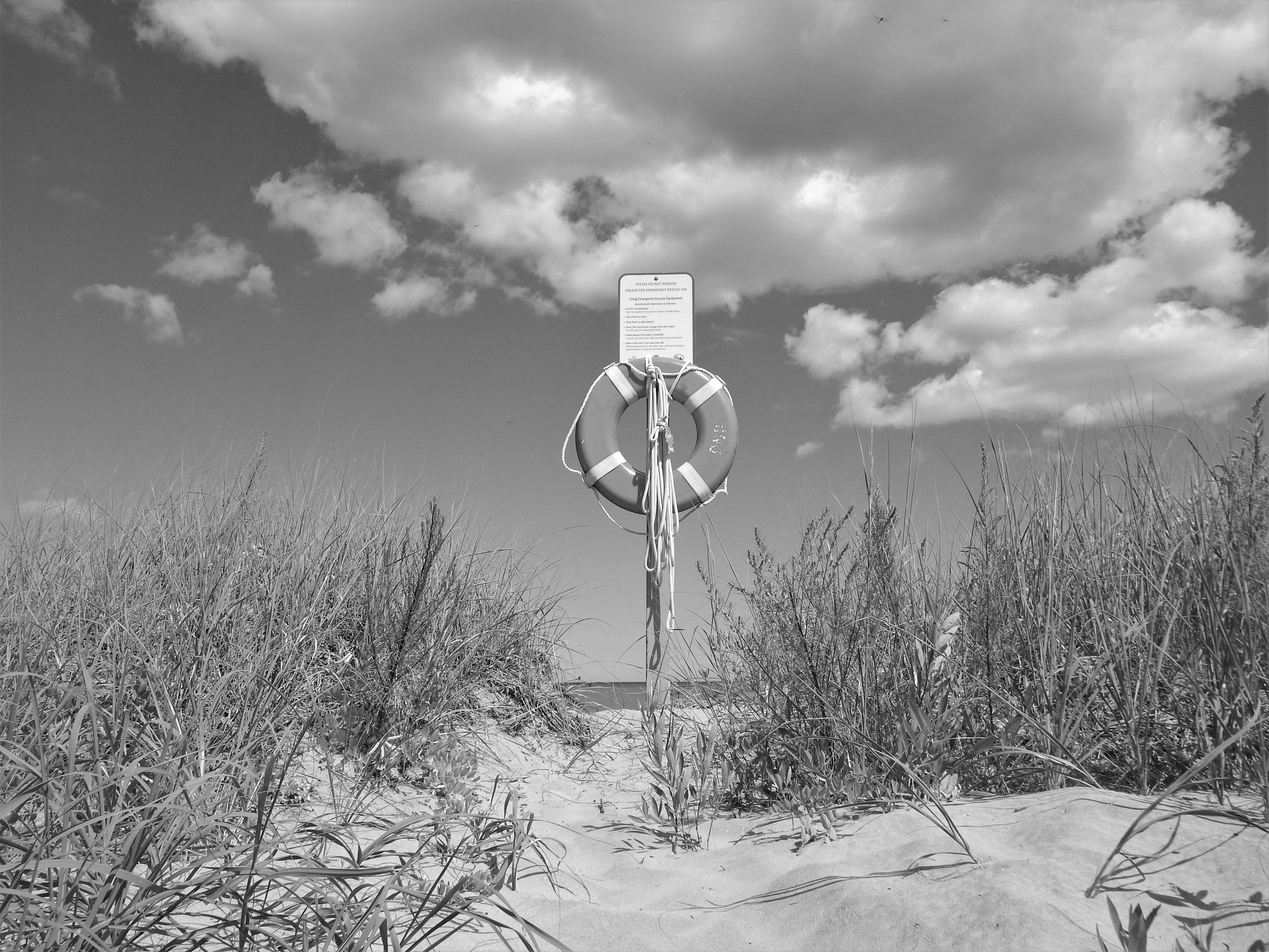 Gratis Svart-hvitt-bilde av livbøye på en sandstrandsti, dramatiske skyer over hodet. Arkivbilde