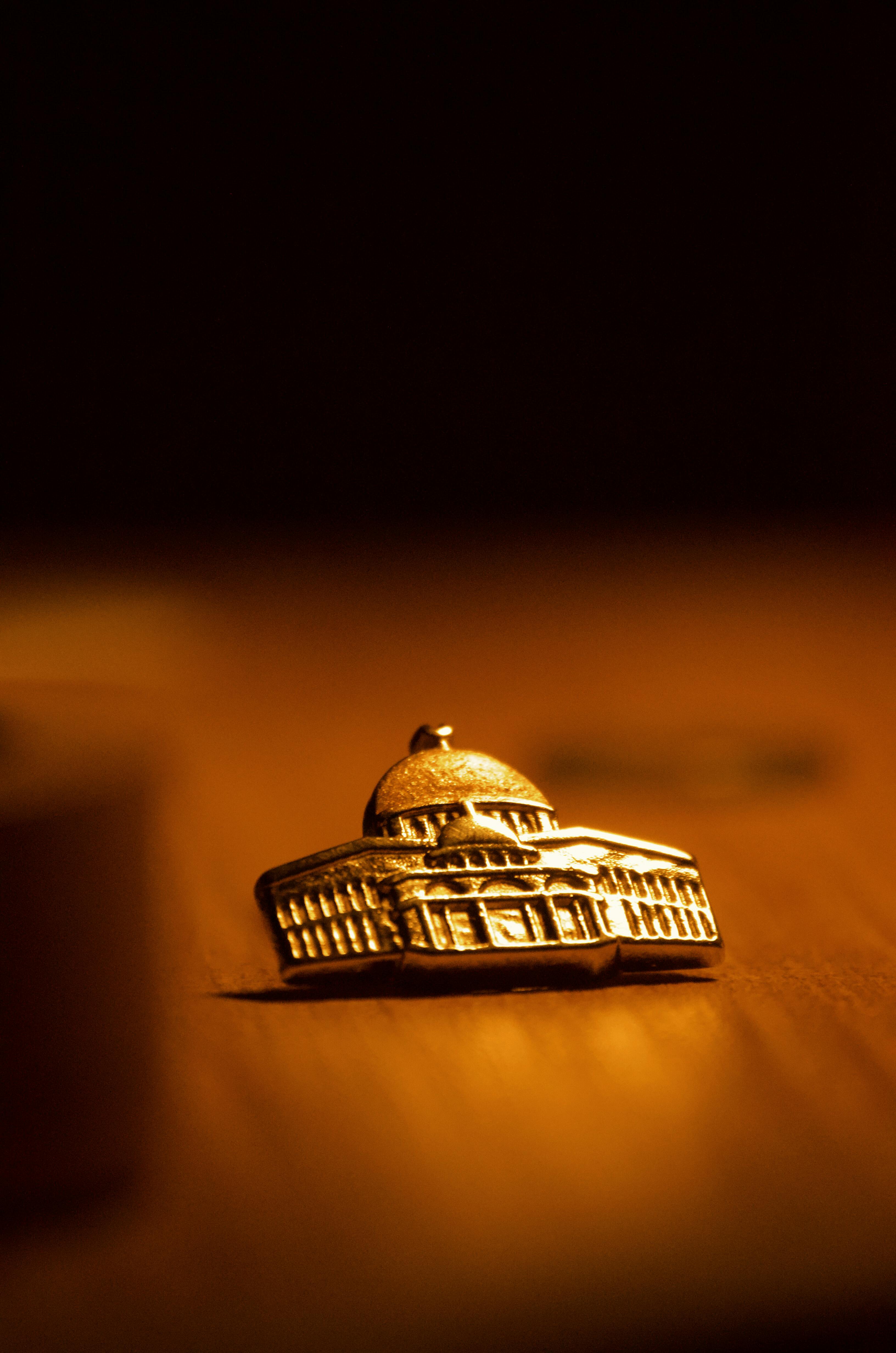 Ücretsiz Ahşap bir yüzey üzerinde sıcak ışık altında çekilmiş, kubbeli altın renkli bir bina hatırasının yakın plan fotoğrafı. Stok Fotoğraflar