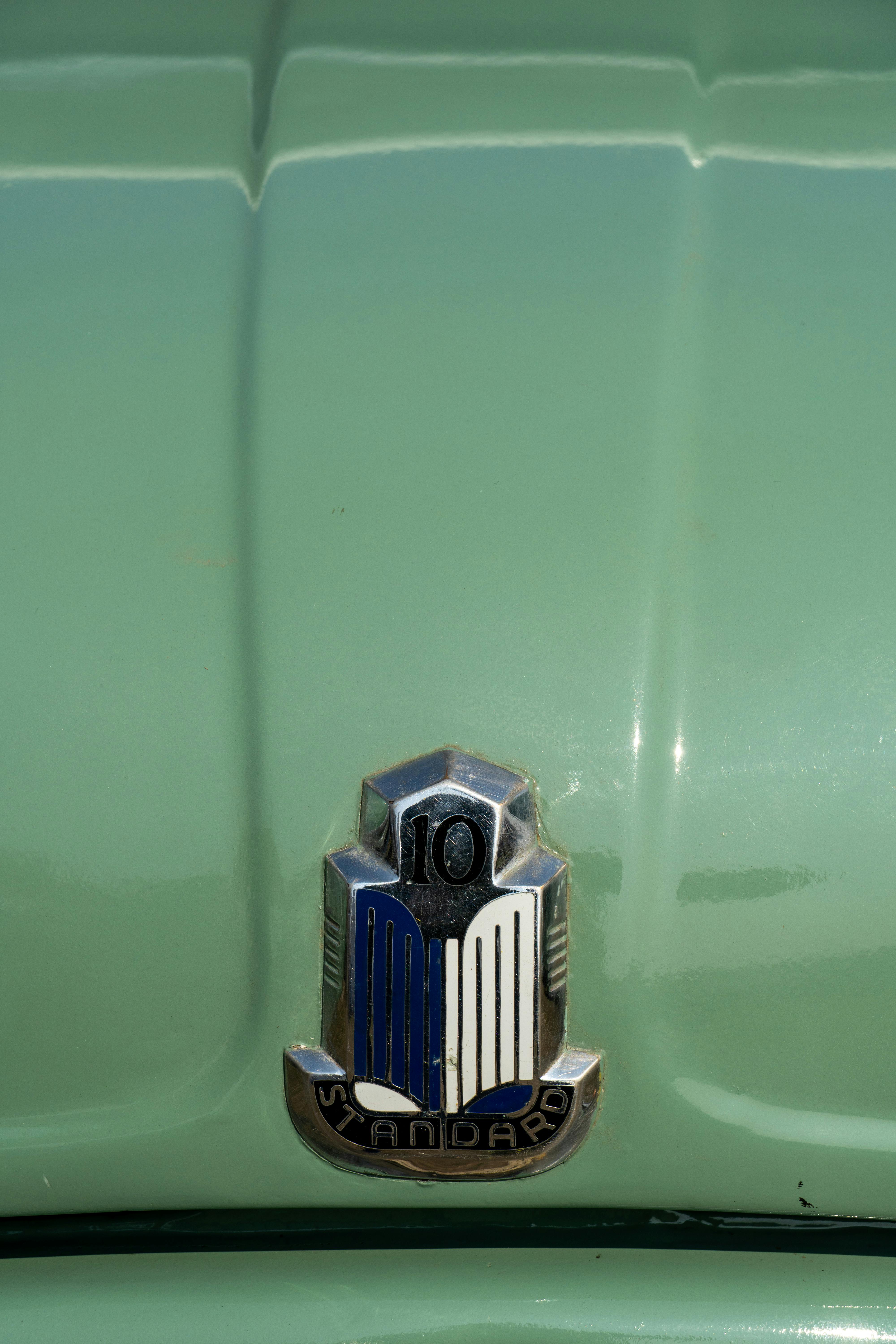 Gratis Primo piano dell'emblema di un'auto d'epoca Standard 10 su sfondo verde menta, che mette in risalto il design automobilistico classico. Foto a disposizione
