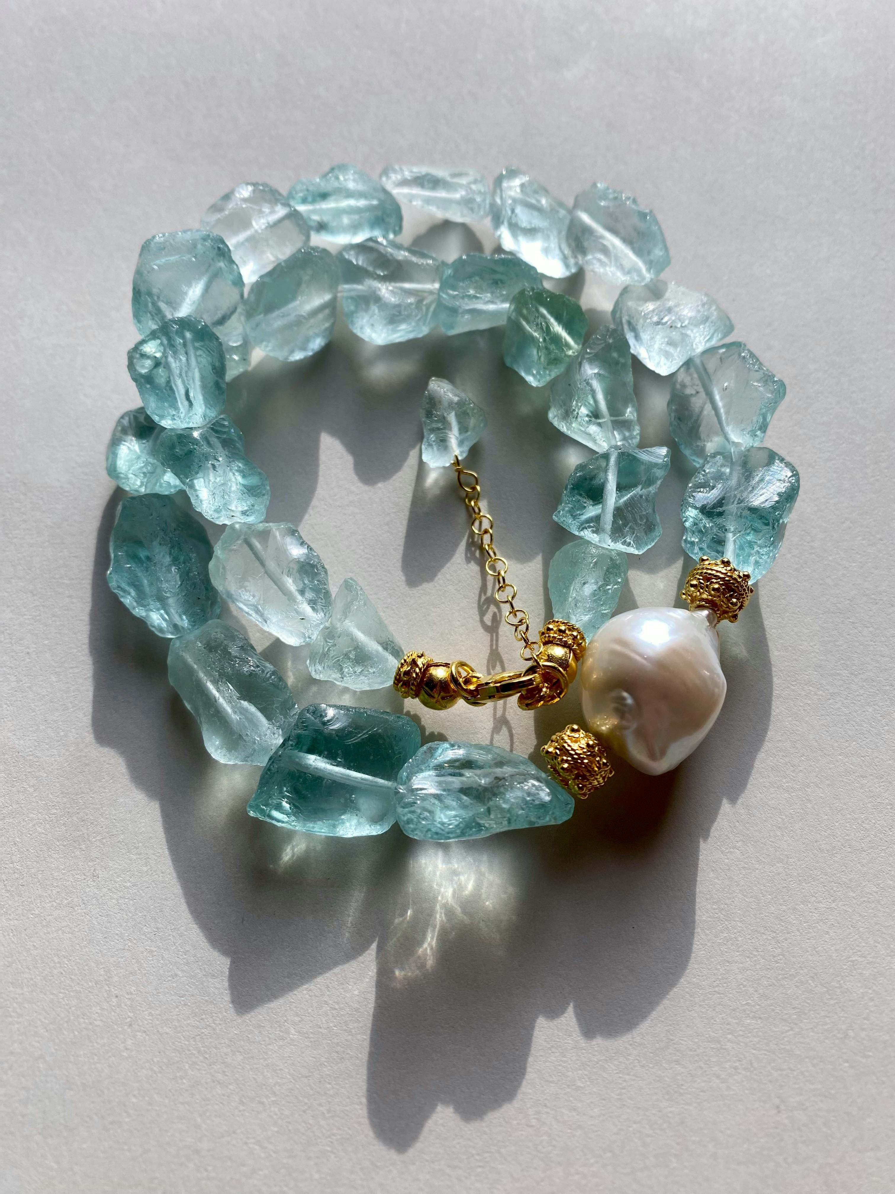 Elegant aquamarine and pearl bracelet with gold accents in soft lighting.