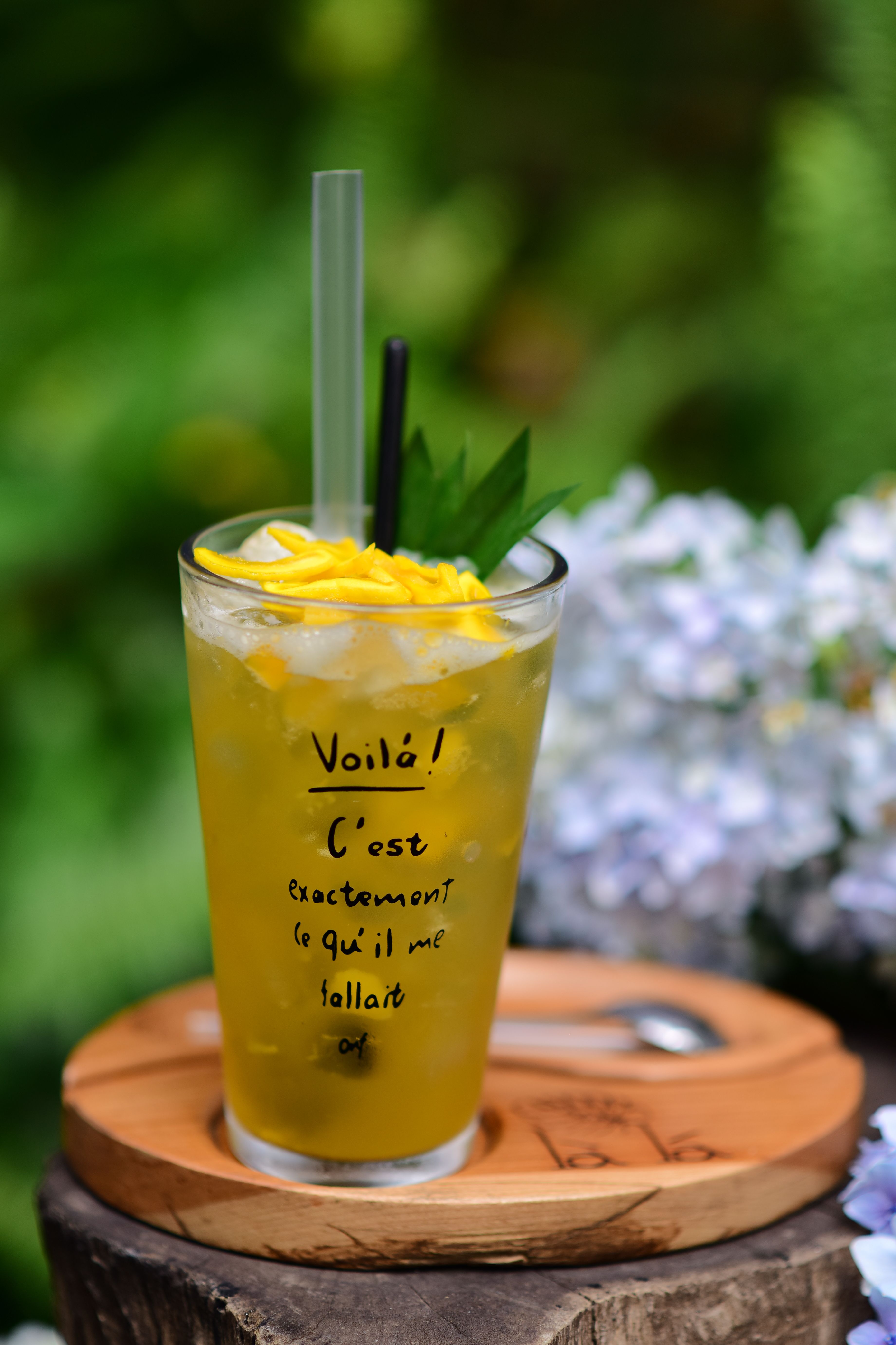 Iced mango drink with floral decor and a rustic wooden coaster.