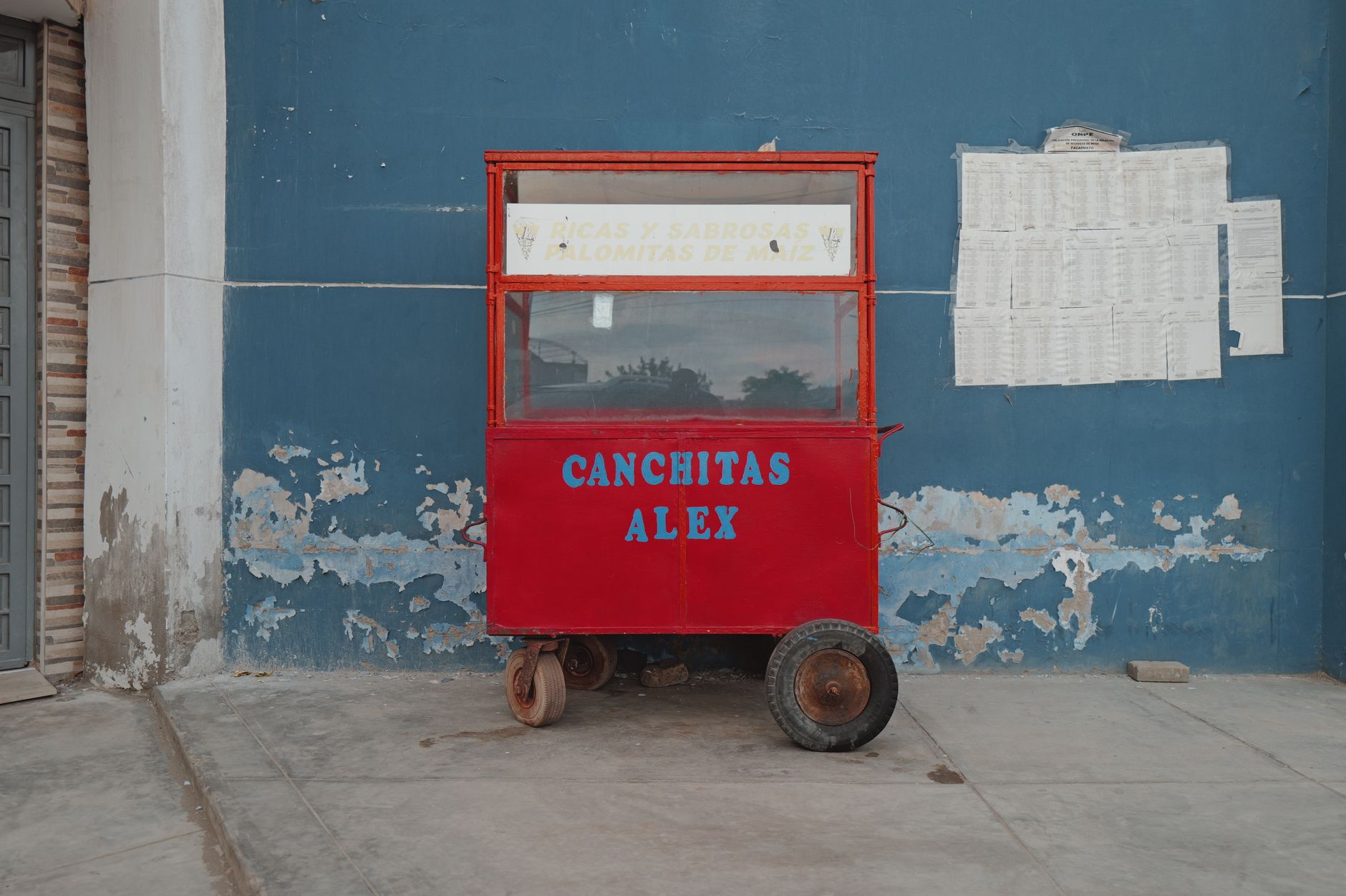 A colorful red popcorn cart against a blue wall, located in Chiclayo, Peru. Perfect for street and travel themes.