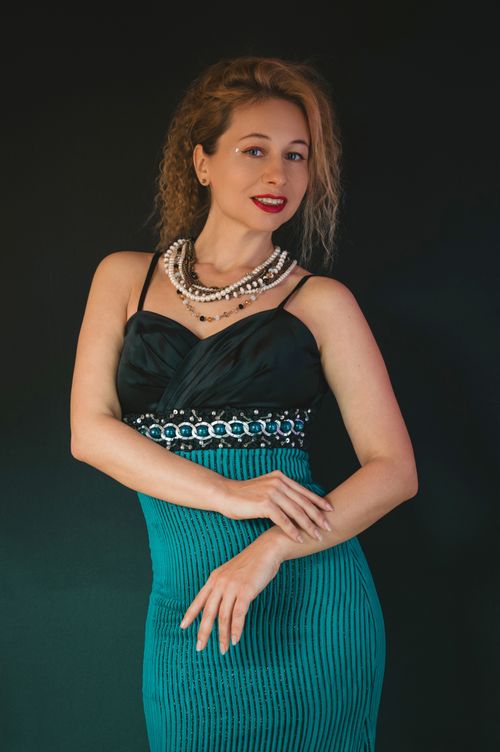 Free Elegant woman with curly hair and pearls posing in a teal dress against dark background. Stock Photo