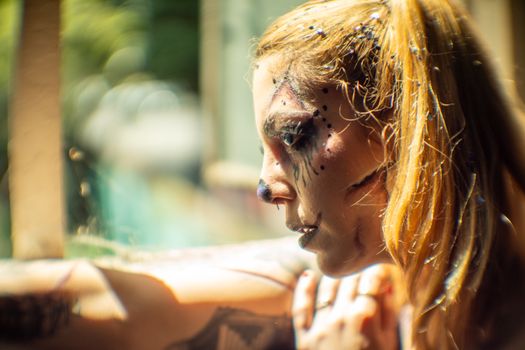 Close-up of woman with artistic Halloween makeup and glitter in bright daylight.