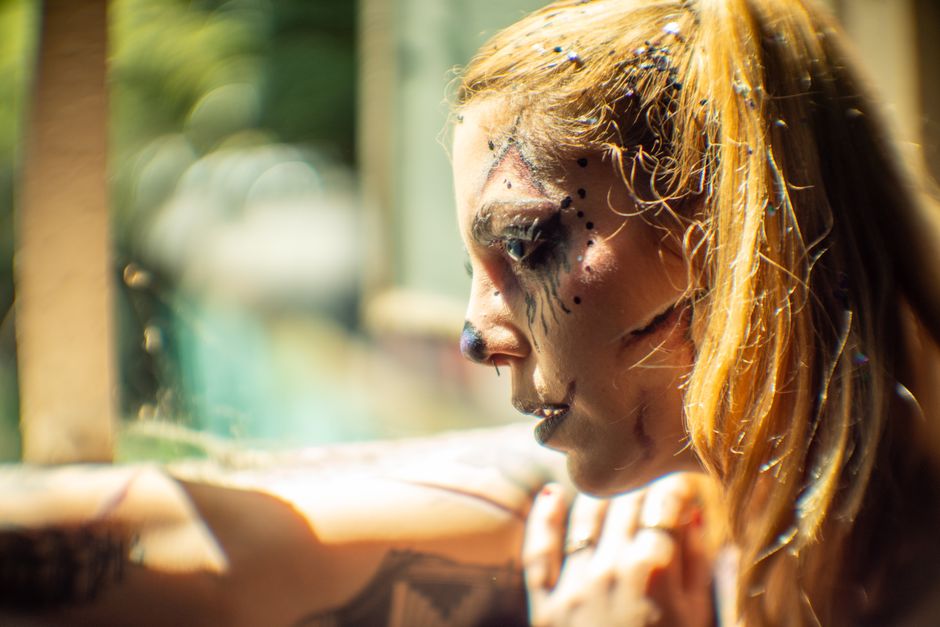 Close-up of woman with artistic Halloween makeup and glitter in bright daylight.