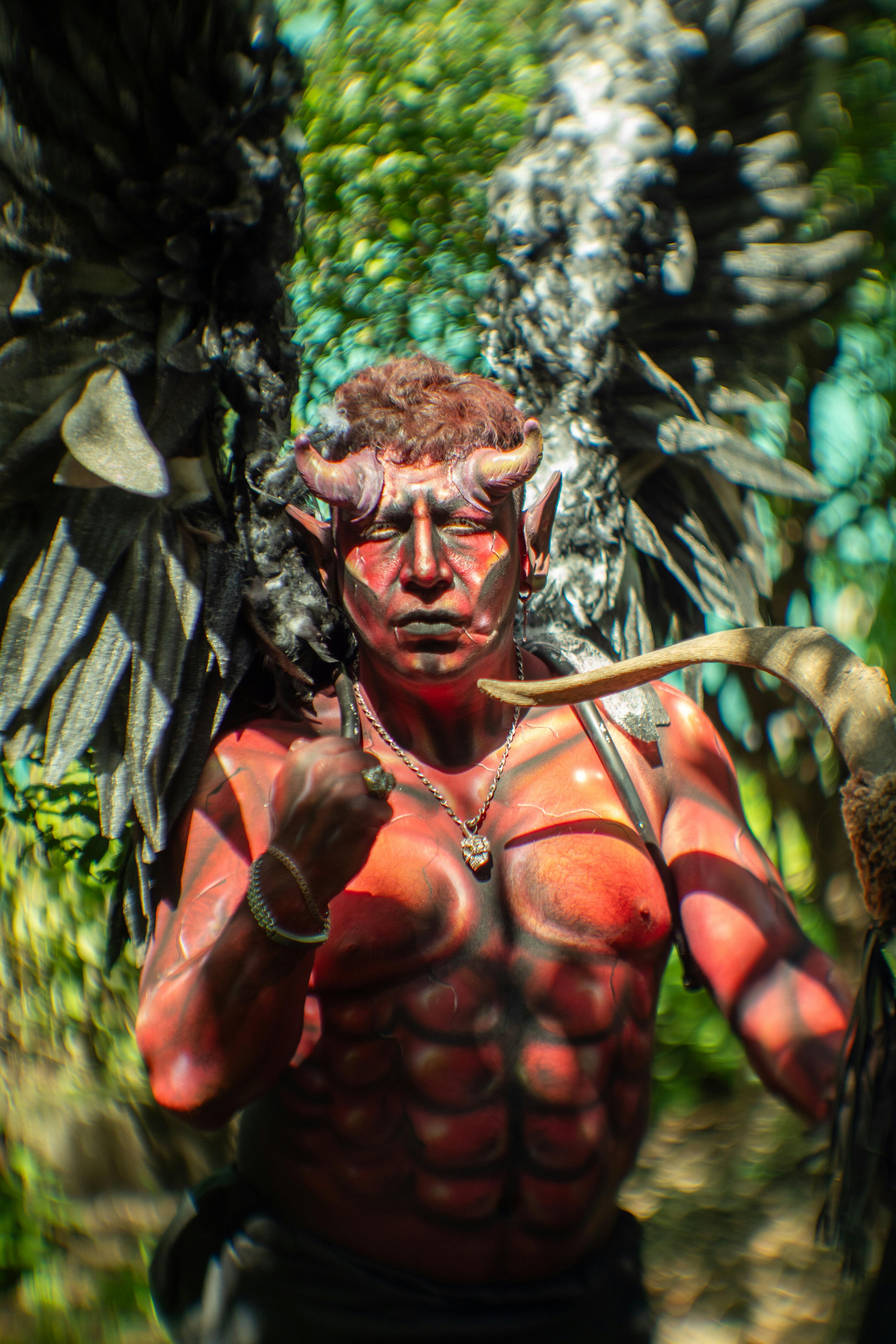 Man in vibrant demon costume with makeup and wings in Mexico City outdoor setting.
