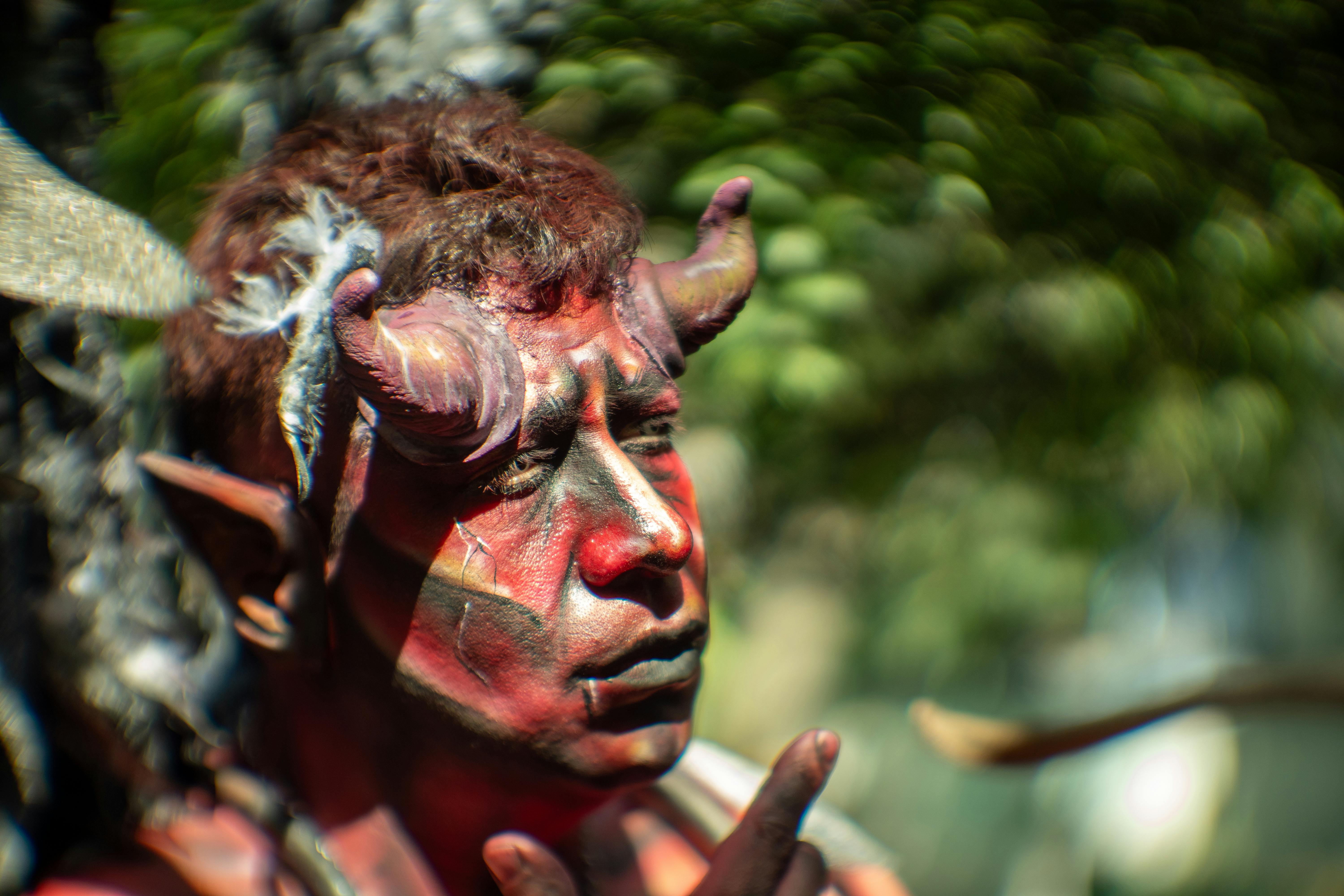 Close-up of a man in a devil costume with intricate makeup and horns, outdoors in Mexico City.