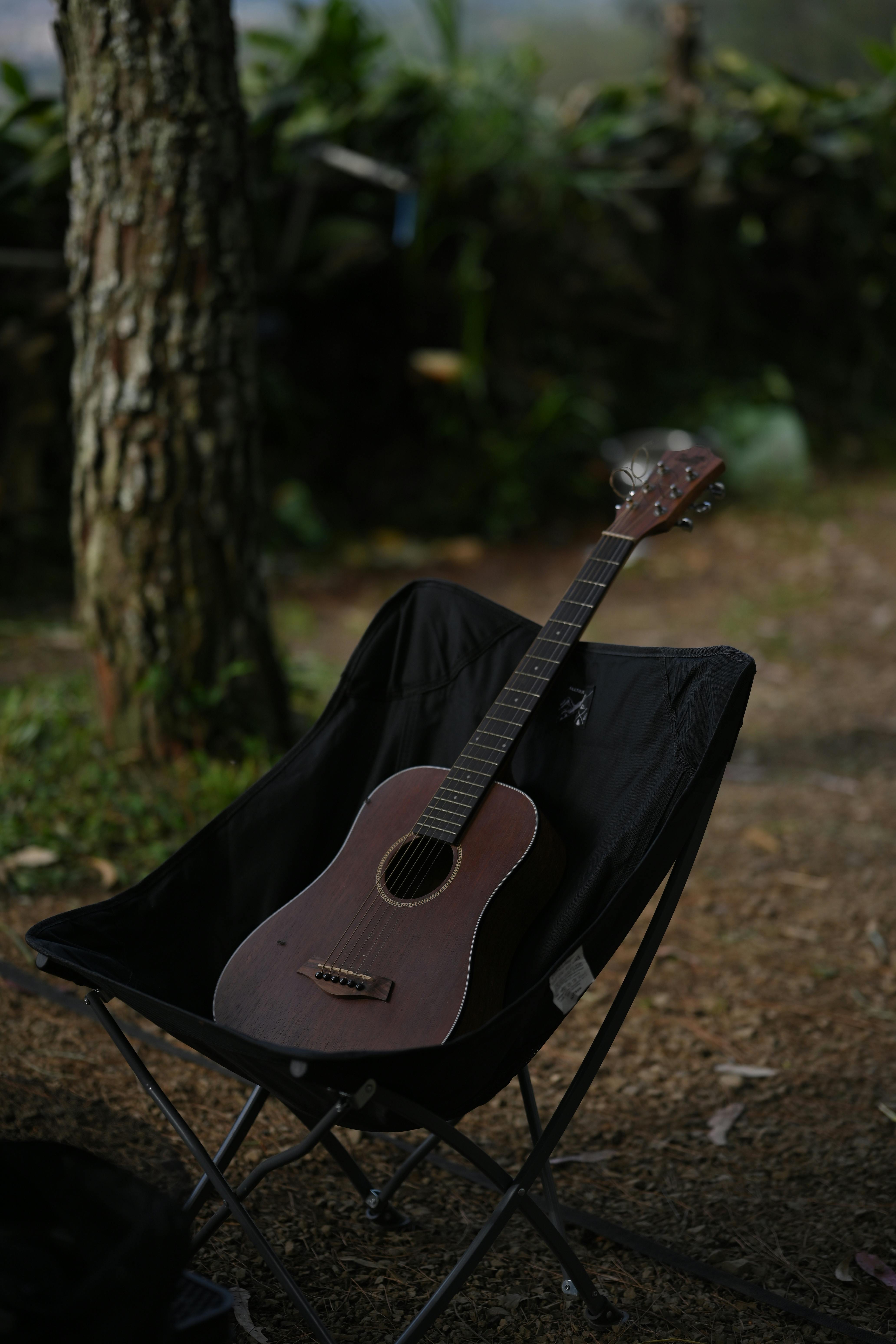 Kostnadsfria Akustisk gitarr vilar på en campingstol mitt i naturlig skogsbakgrund i Bandung. Stock foto