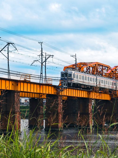 Free Train travels on an iconic orange bridge in Wakayama, Japan under a vibrant blue sky. Stock Photo