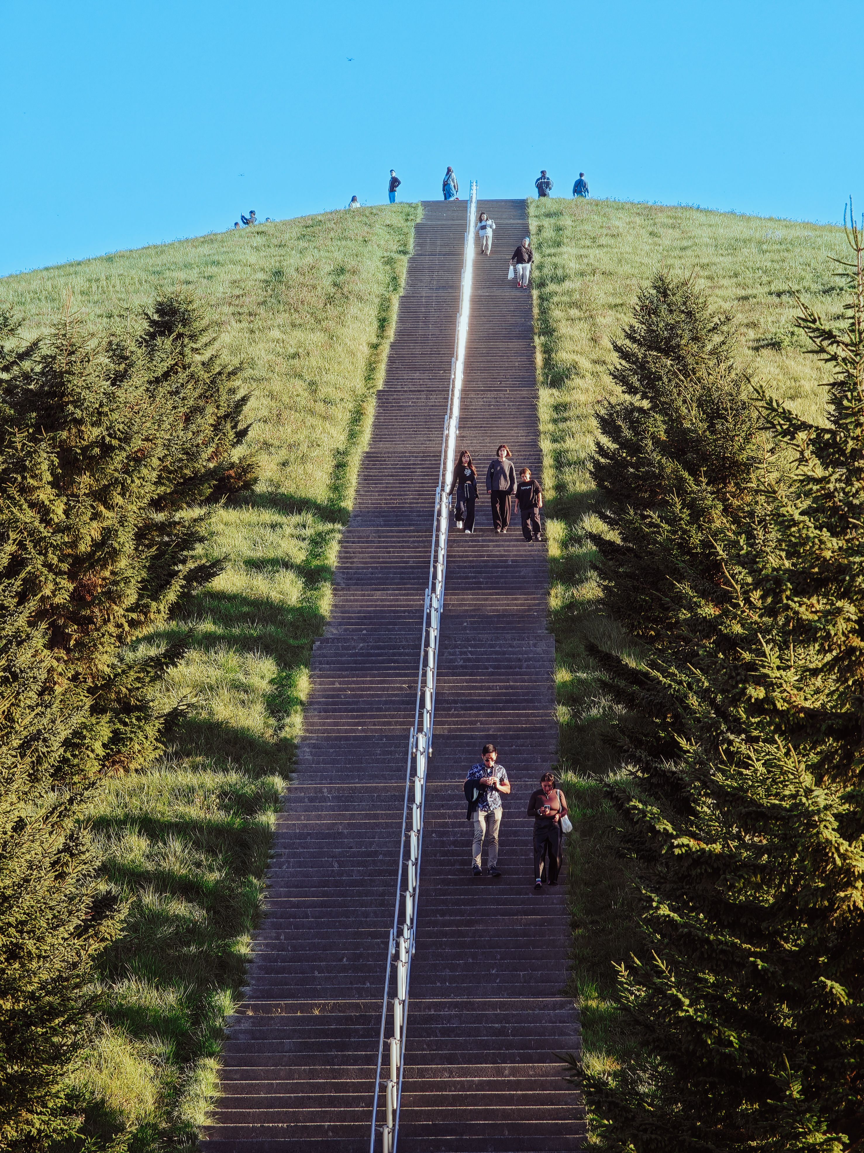 A grassy hill with a large staircase where people are climbing under a clear blue sky.