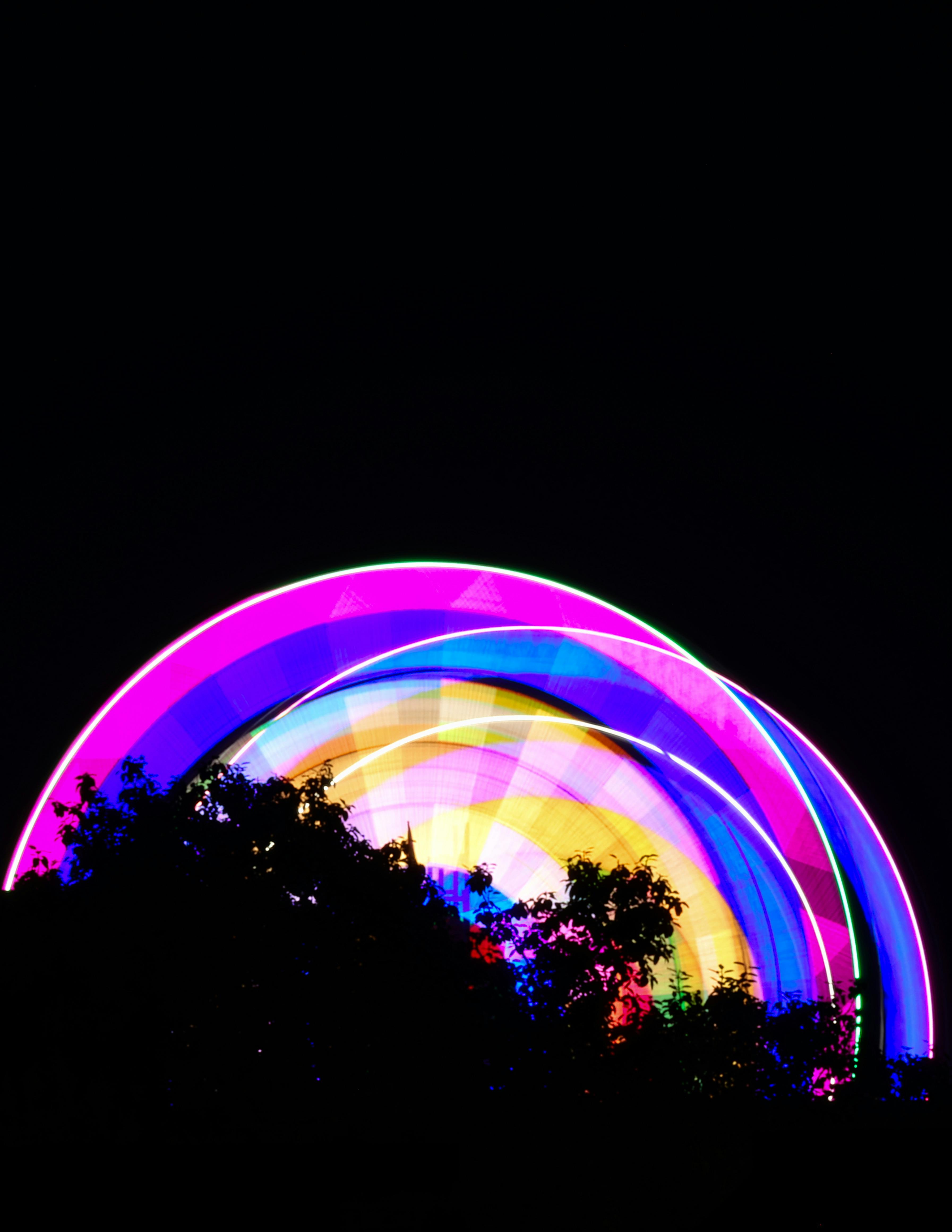 Kostenlos Ein farbenprächtig beleuchtetes Riesenrad dreht sich vor dunklem Nachthimmel und erzeugt leuchtende Lichtspuren. Stock-Foto