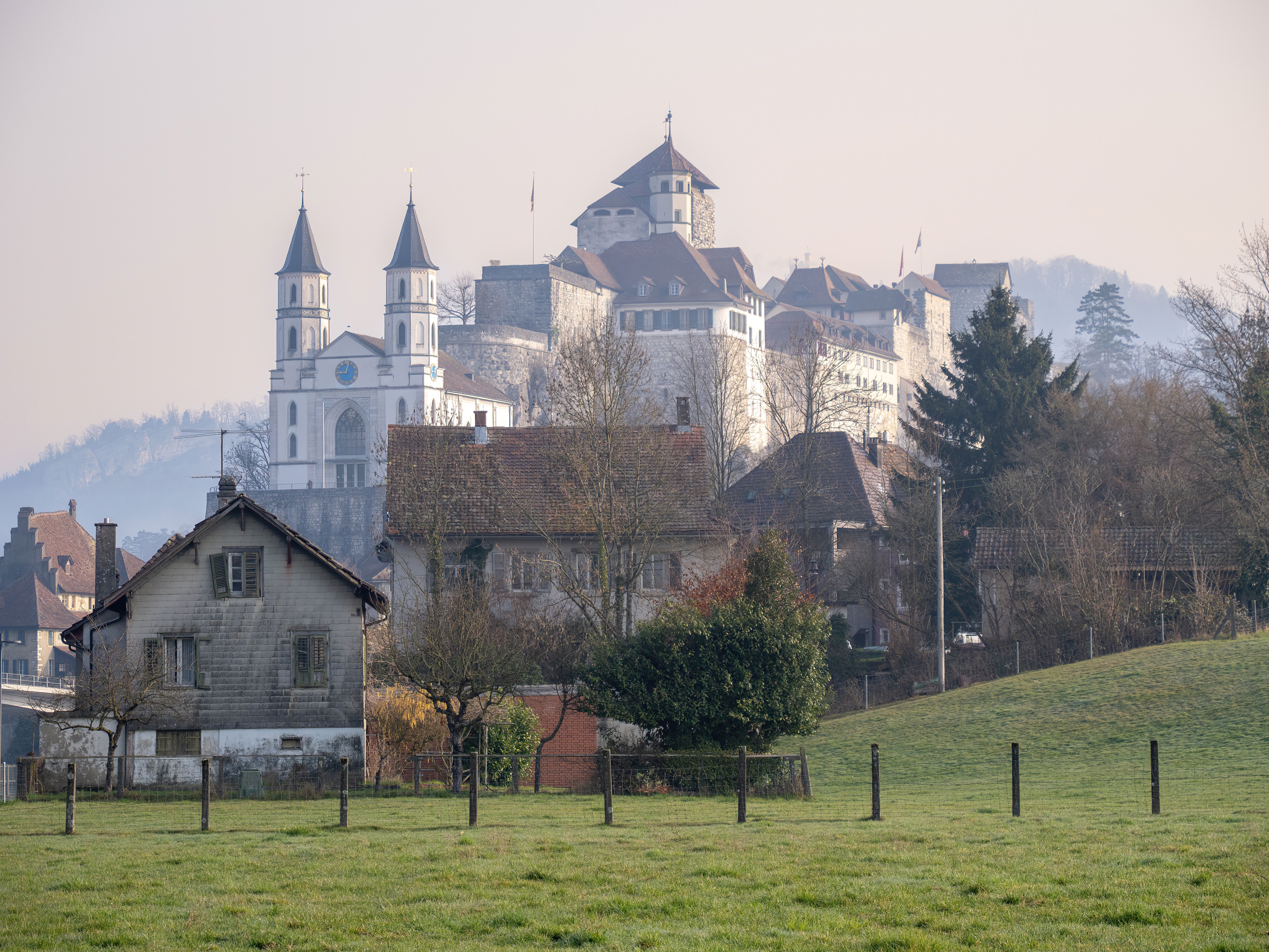 Picturesque view of a historic Swiss castle surrounded by misty winter scenery.
