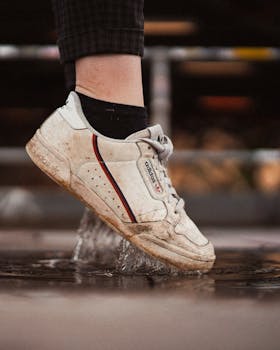 Close-up of a dirty sneaker splashing through a puddle in a city setting.