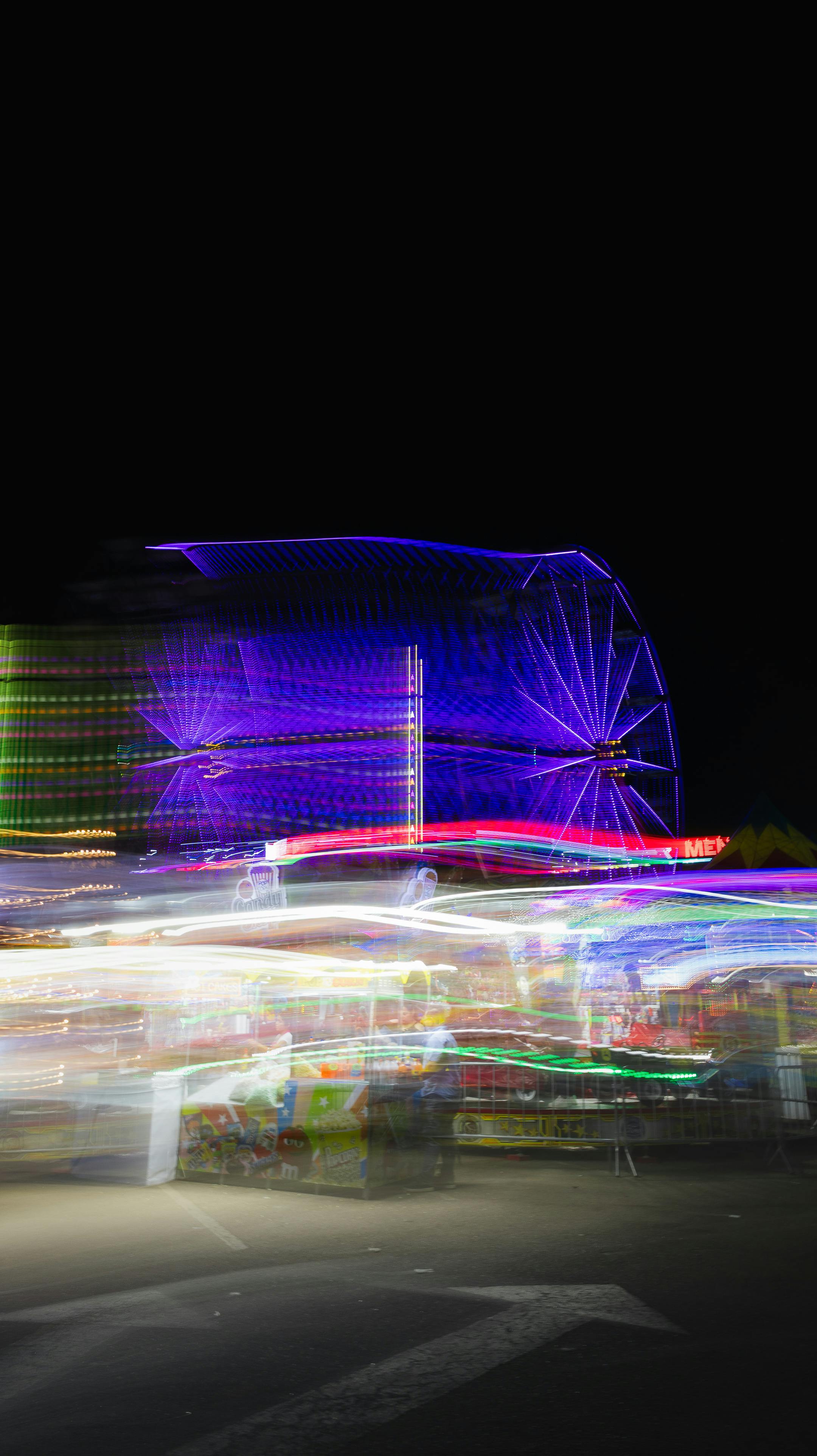Free Long exposure shot capturing a colorful Ferris wheel at a nighttime carnival with vibrant lights. Stock Photo