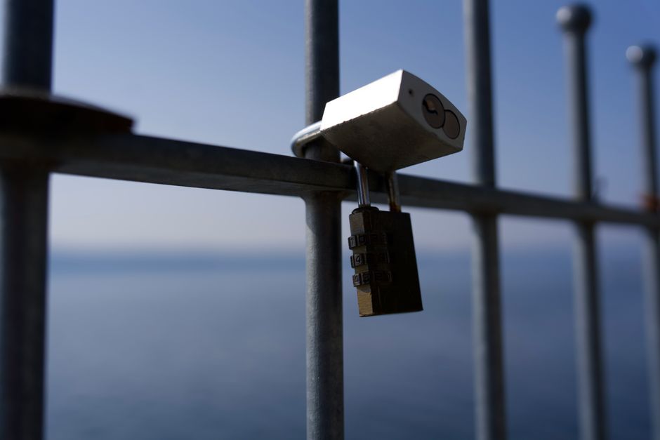 Secure padlock hanging on a metal fence with a serene sea view in the background.