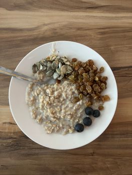 Nutritious oatmeal with seeds, raisins, and blueberries on a wooden table.