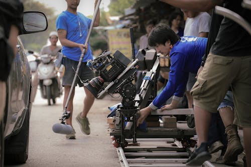 Man in Blue Shirt and Brown Pants Holding A Camera Equipment