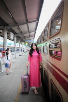 Woman in pink dress standing next to train with suitcase, ready for travel.