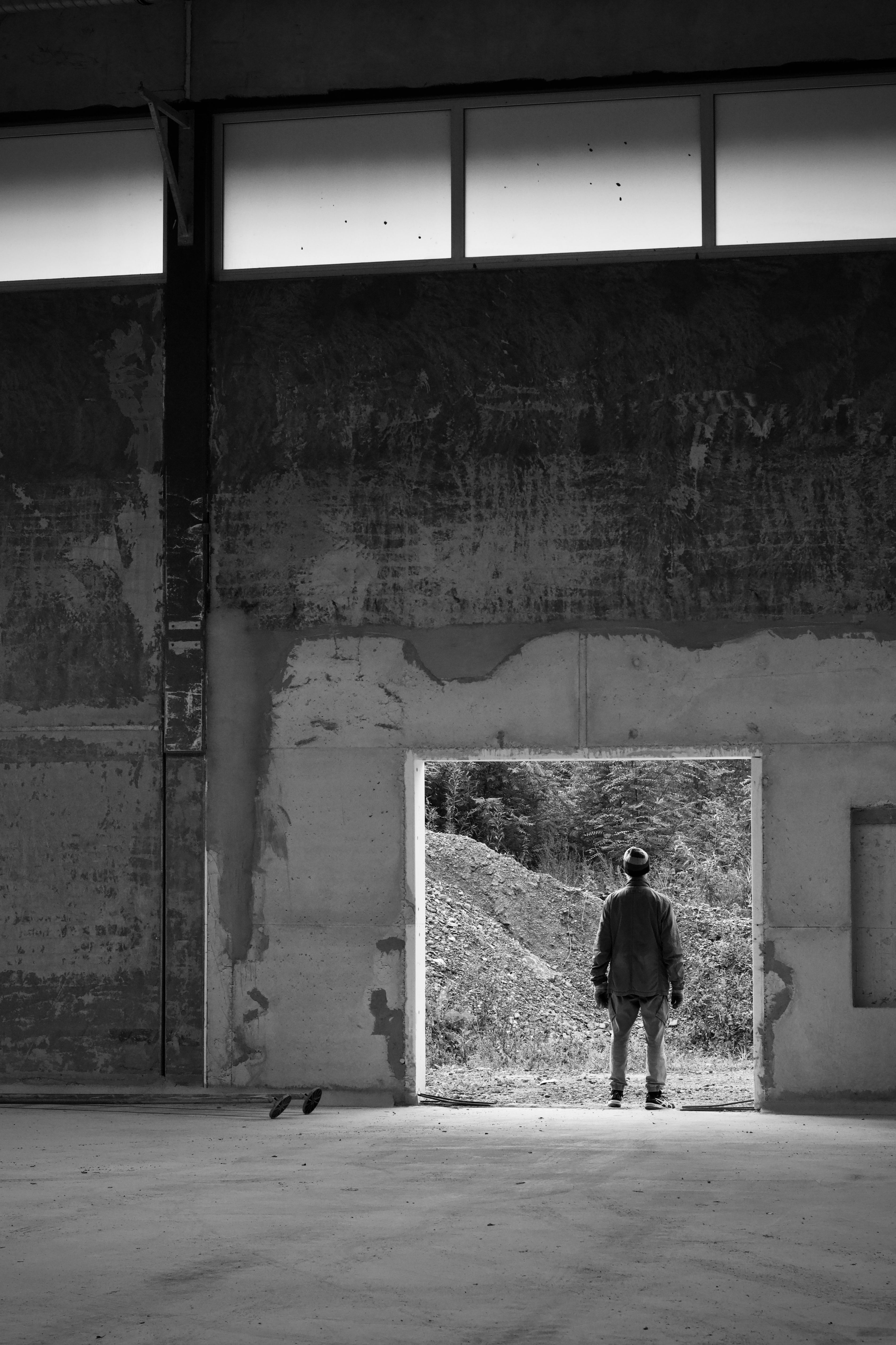 Fotomural Una persona solitaria se encuentra en la entrada de un edificio industrial abandonado, mirando hacia afuera.