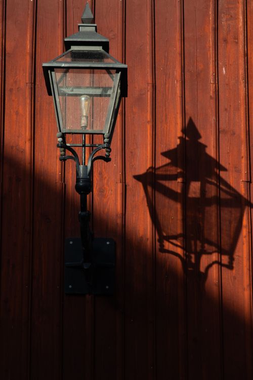 Free Historic street lamp casting a shadow on a rustic red wooden wall in Jönköping, Sweden. Stock Photo