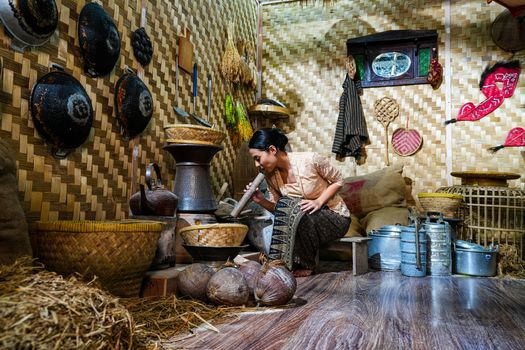 A woman prepares food using traditional tools in a rustic Indonesian kitchen setting. - Fotografer Sidoarjo