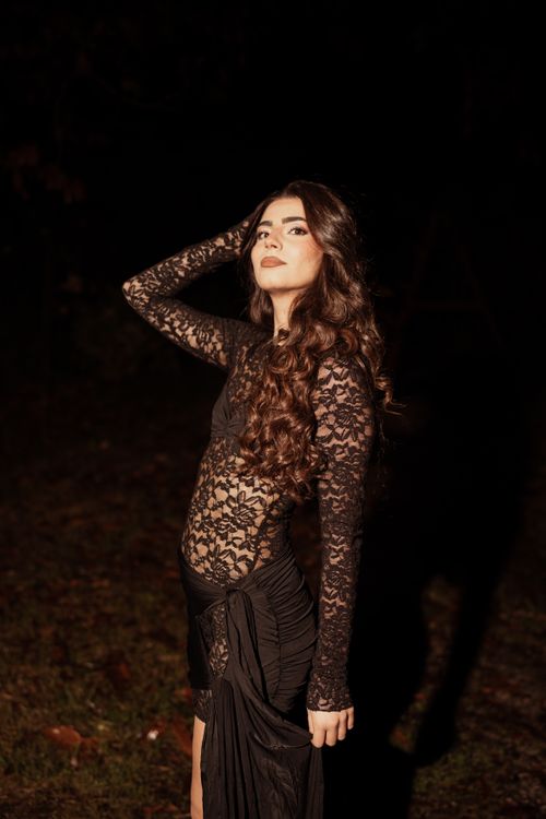 Free A striking portrait of a woman in a black lace dress posing confidently outdoors at night. Stock Photo