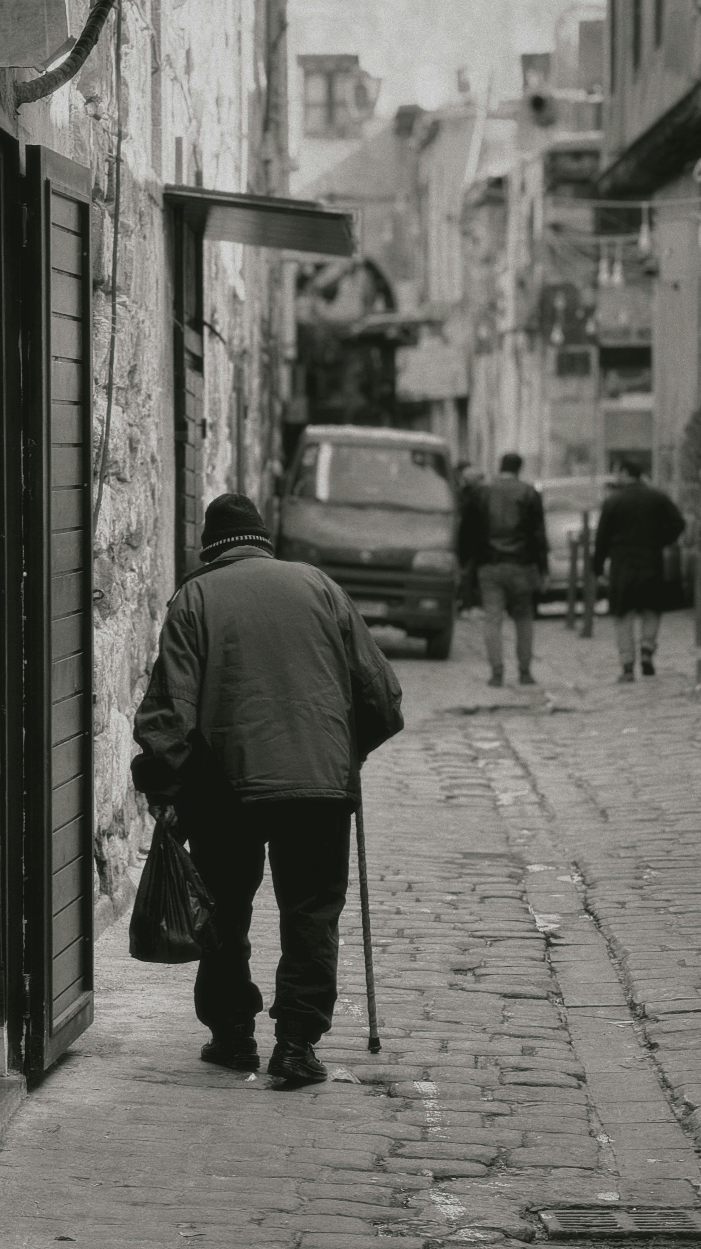 Elderly man with cane walking in an old Damascus street, reflecting urban life and solitude.