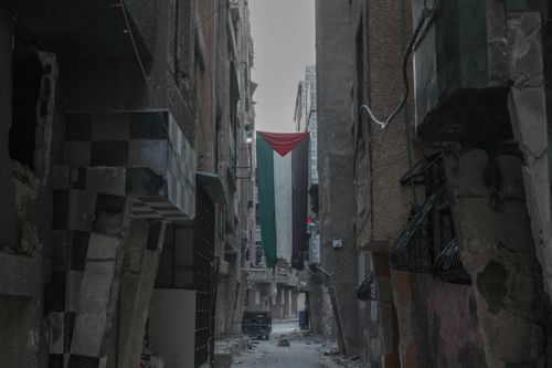 Free War-torn alley in Damascus featuring a large Syrian flag. Stock Photo