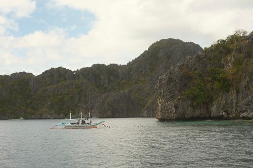 Free A traditional Filipino boat floats in El Nido's scenic bay, surrounded by limestone cliffs. Stock Photo