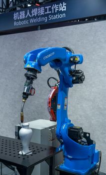 Industrial robotic welding station featuring a blue robot arm welding a metal object.