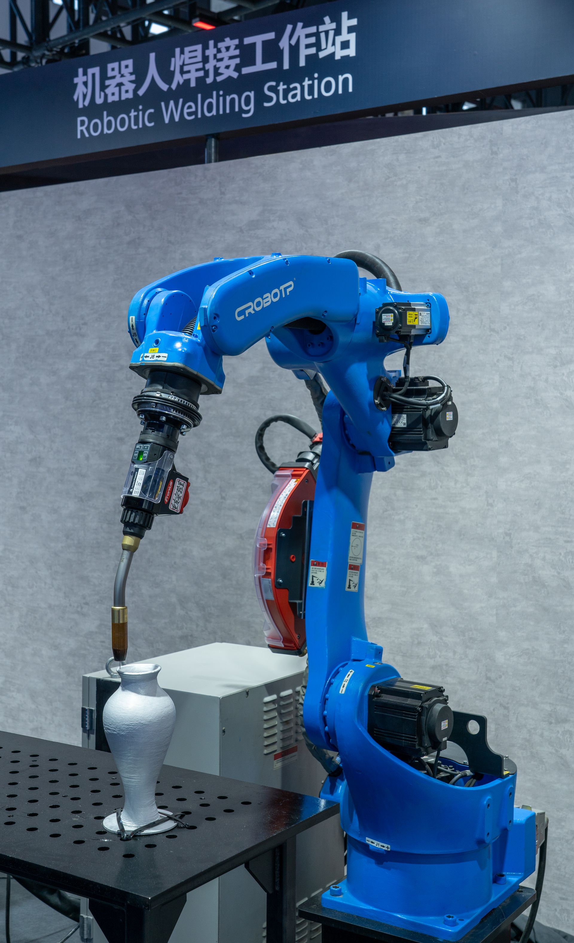 Industrial robotic welding station featuring a blue robot arm welding a metal object