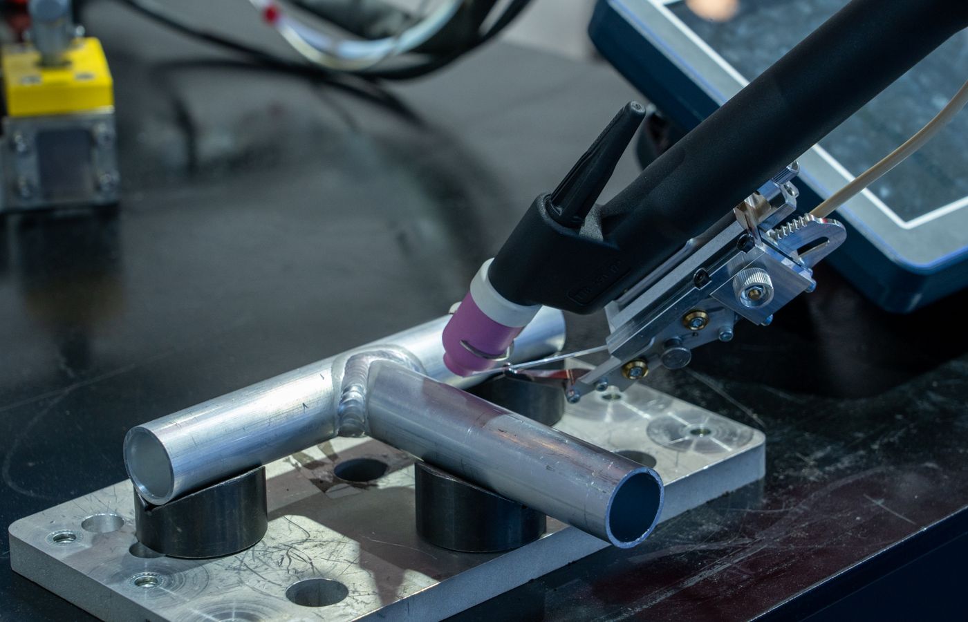 Close-up of a welding torch creating a weld bead on a metal joint at an industrial workbench