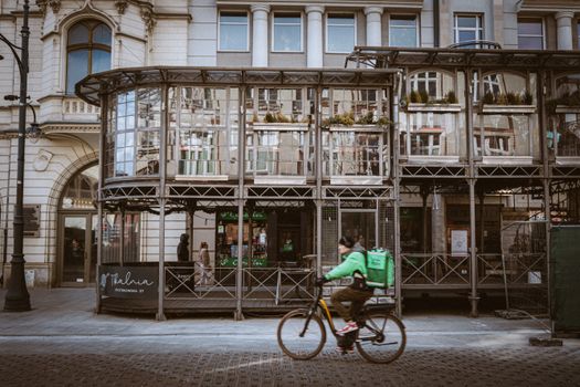Cyclist passes by an architectural landmark on Piotrkowska Street, Łódź, Poland.