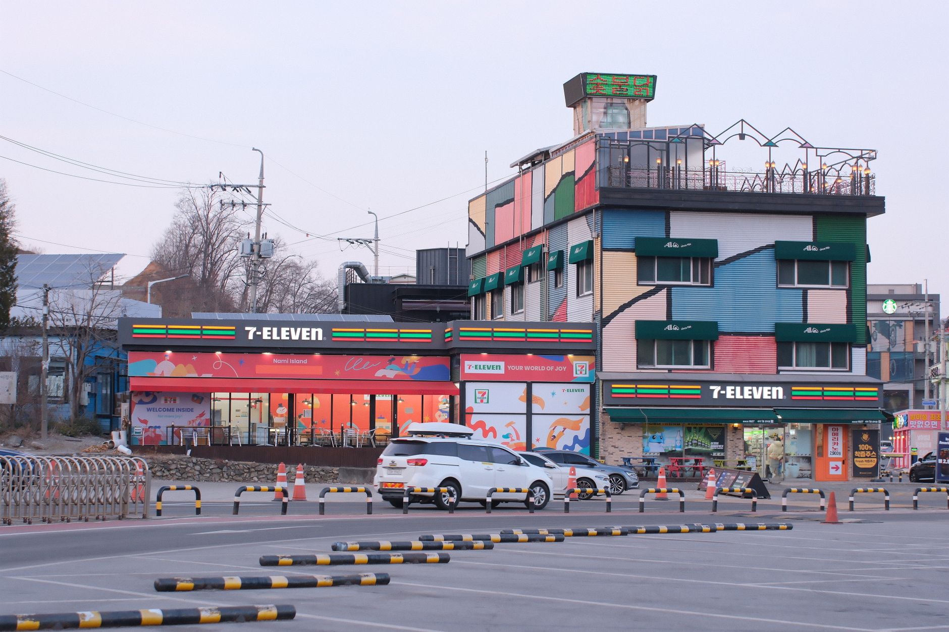 A vibrant 7-Eleven store with colorful facade and parking lot in the foreground, during daytime.