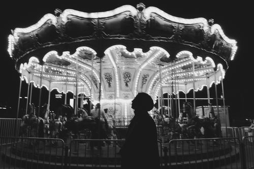 Free A person silhouetted against a brightly lit carousel at night creates a nostalgic and whimsical scene. Stock Photo