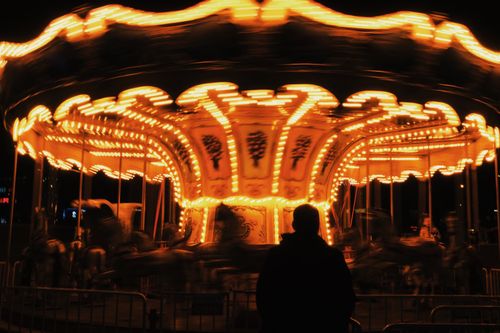 Free Silhouette of man watching a brightly lit carousel spinning at night. Stock Photo