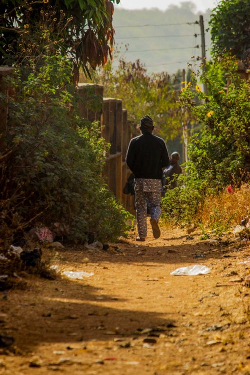 Free A man walking along a narrow, rustic dirt pathway flanked by greenery on a sunny day. Stock Photo