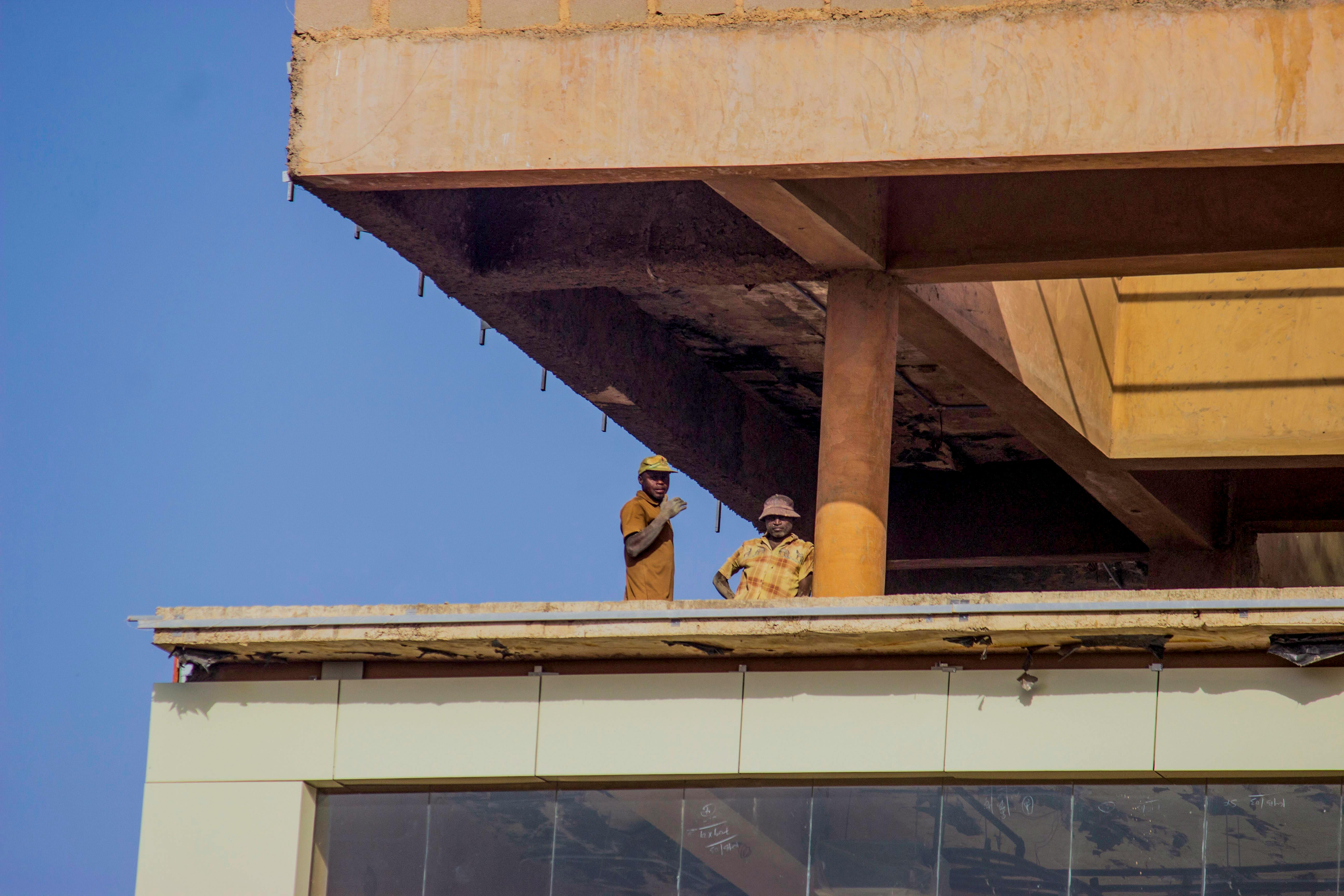 Zadarmo Dvaja stavební robotníci stojaci na budove pod jasnou modrou oblohou. Fotka z fotobanky