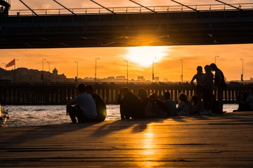 Free Silhouettes of people relaxing by the water as the sun sets, creating a serene and warm ambiance. Stock Photo