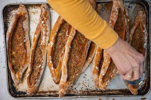 Free Freshly baked Turkish pide being garnished on a baking tray, showcasing traditional cuisine. Stock Photo