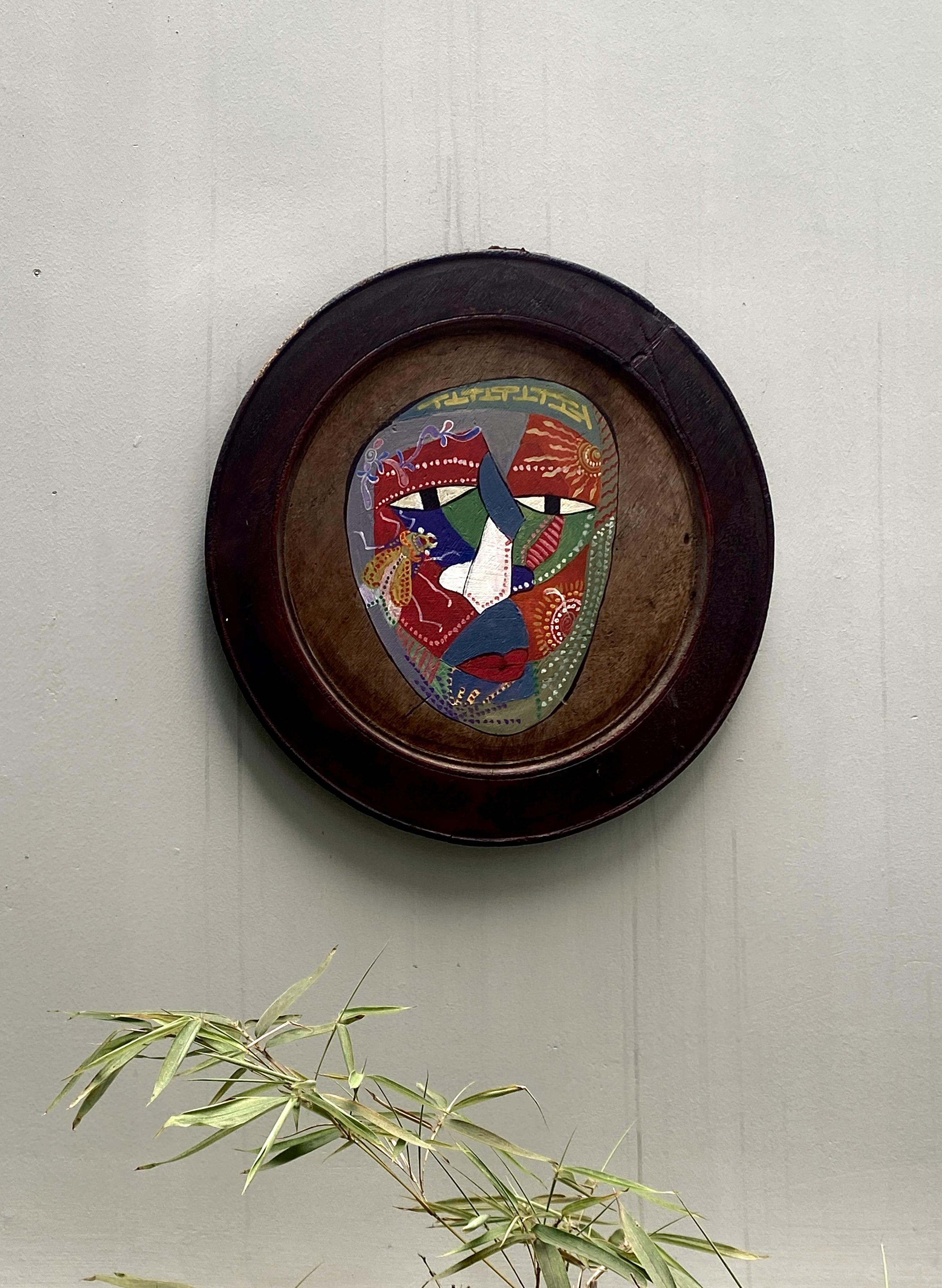 Free Vibrant abstract painting in a round wooden frame on a plain wall with nearby bamboo leaves. Stock Photo