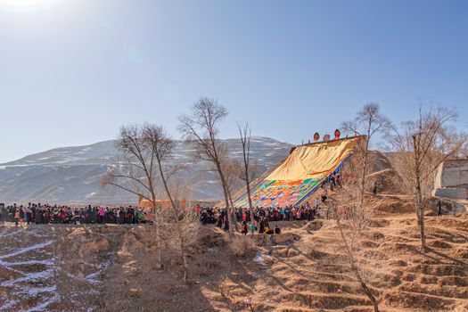 A vibrant cultural event with a large yellow tarp in Huangnan Tibetan Autonomous Prefecture.