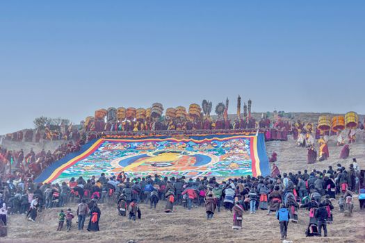 A vibrant Buddhist ceremony at a hillside in Huangnan, Qinghai, China, featuring a large thangka.