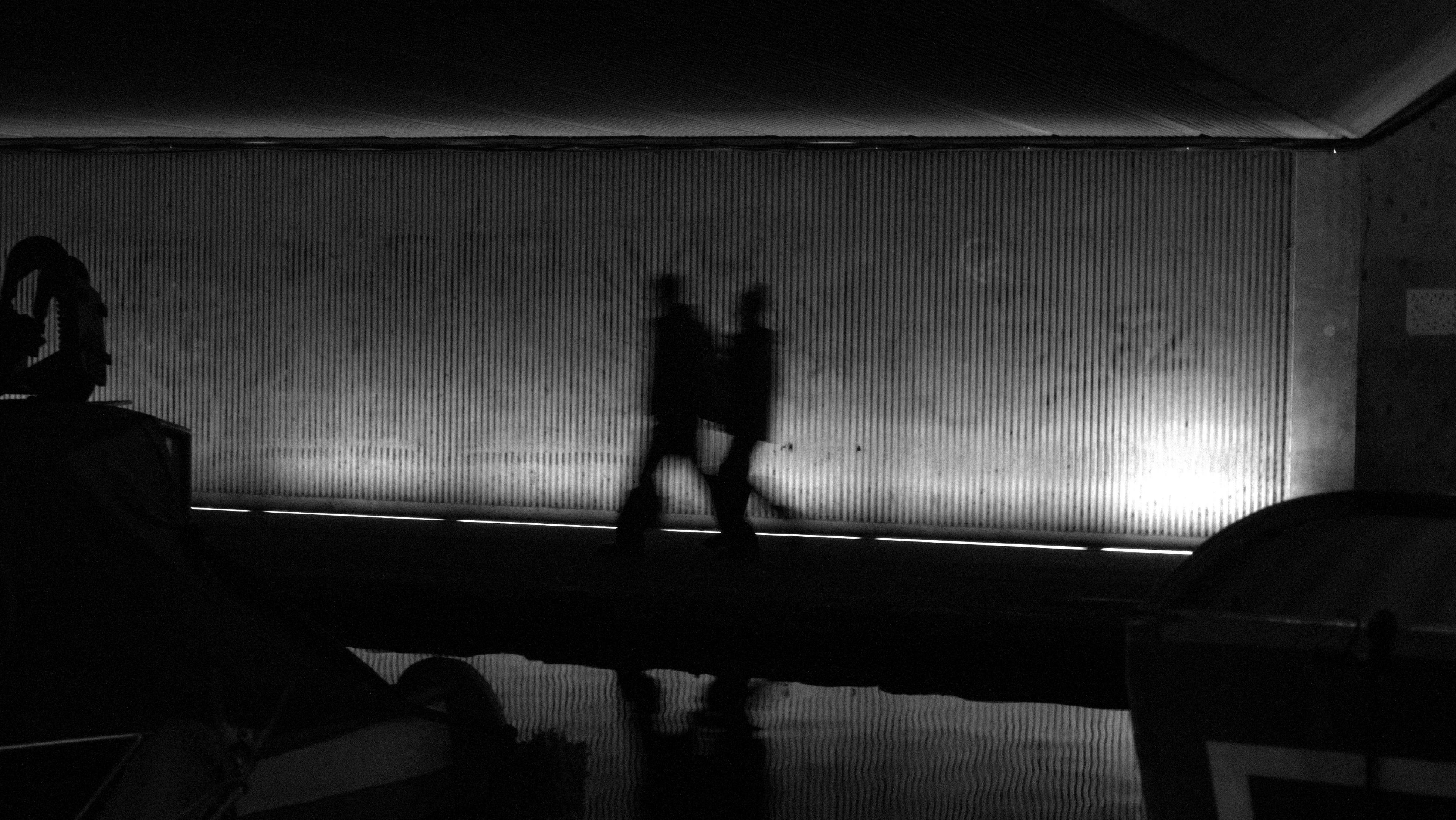 Gratis Siluetas en blanco y negro de dos personas caminando bajo un puente, con una iluminación dramática. Foto de stock
