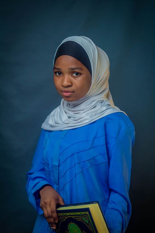 Free Portrait of a young girl wearing a hijab, holding a book, with a calm expression. Stock Photo