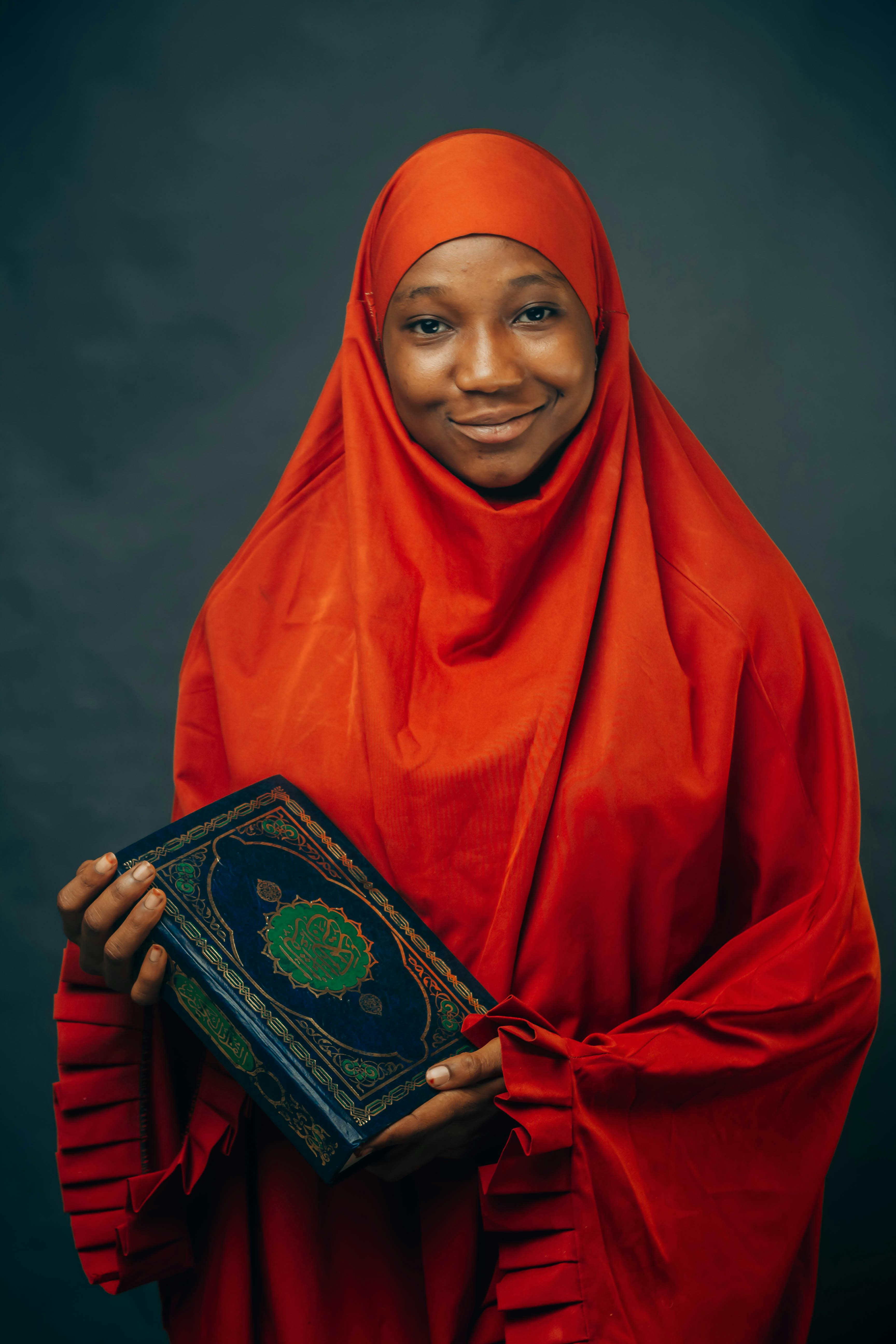 A woman in a red hijab holding a Quran, symbolizing faith and spirituality.
