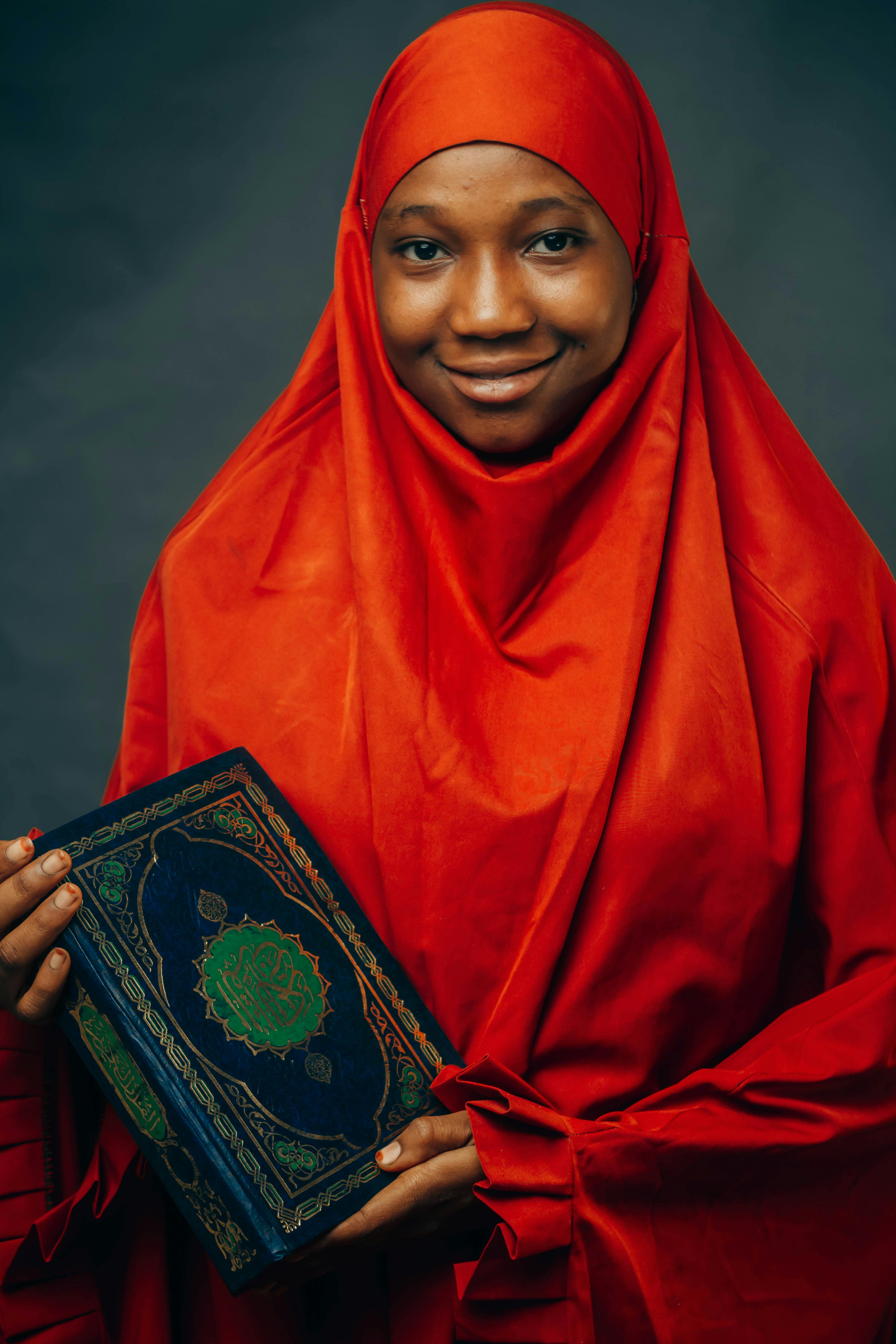 A woman in a vibrant red hijab holding the Quran, symbolizing faith and tradition.