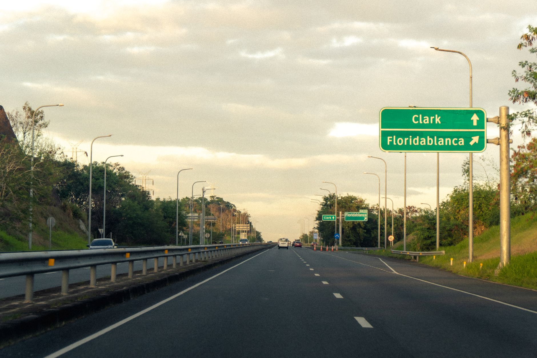 Scenic highway view with road signs pointing to Clark and Floridablanca under a partly cloudy sky.