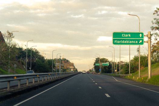 Scenic highway view with road signs pointing to Clark and Floridablanca under a partly cloudy sky.